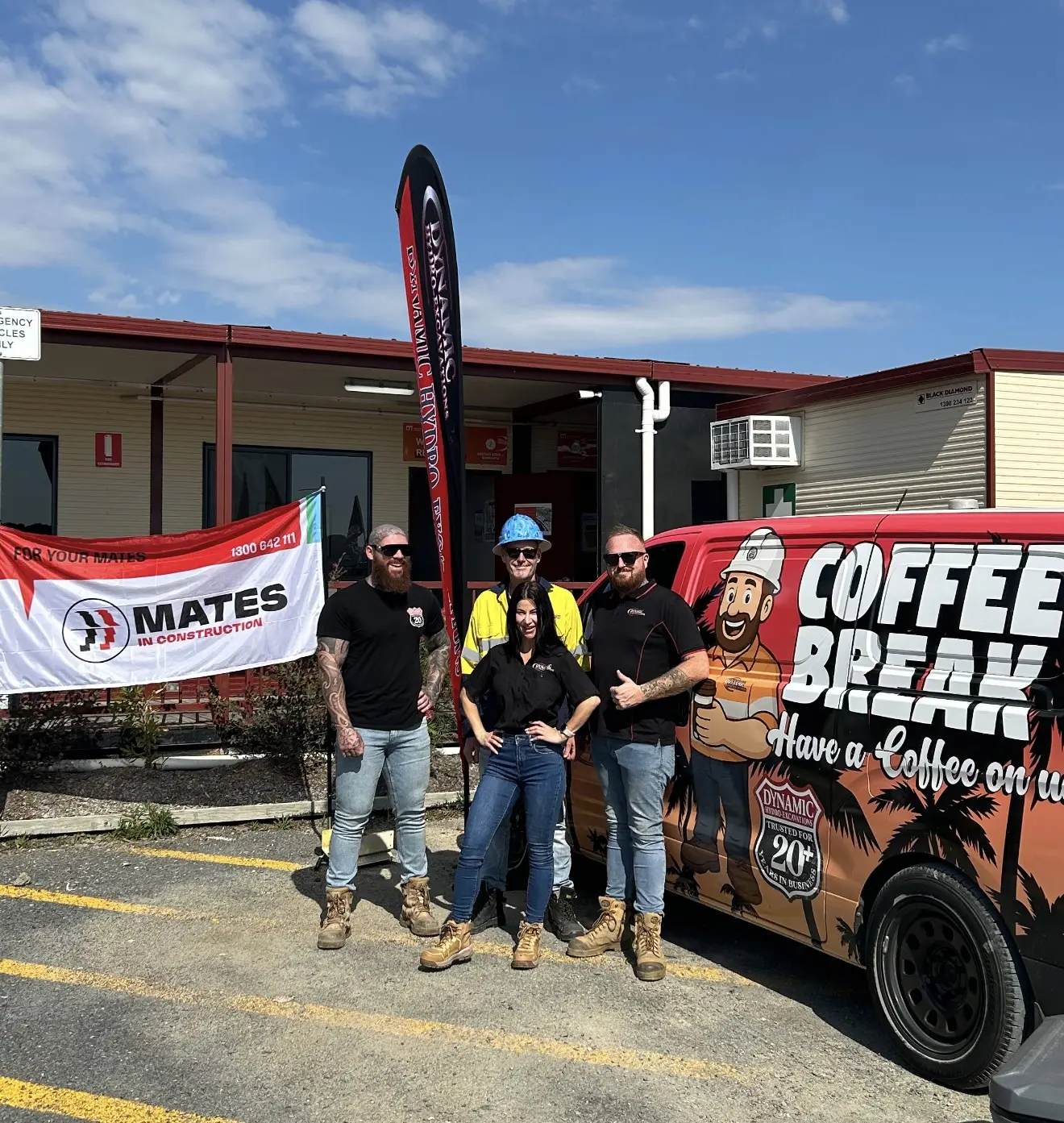 Dynamic team members standing beside the Coffee Break van at a site office, next to a MATES in Construction banner and a Dynamic flag
