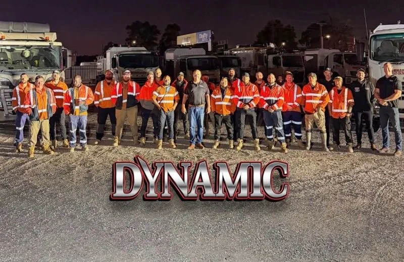 Dynamic Hydro Excavations crew in high-visibility clothing lined up in front of a row of trucks at the depot at dusk