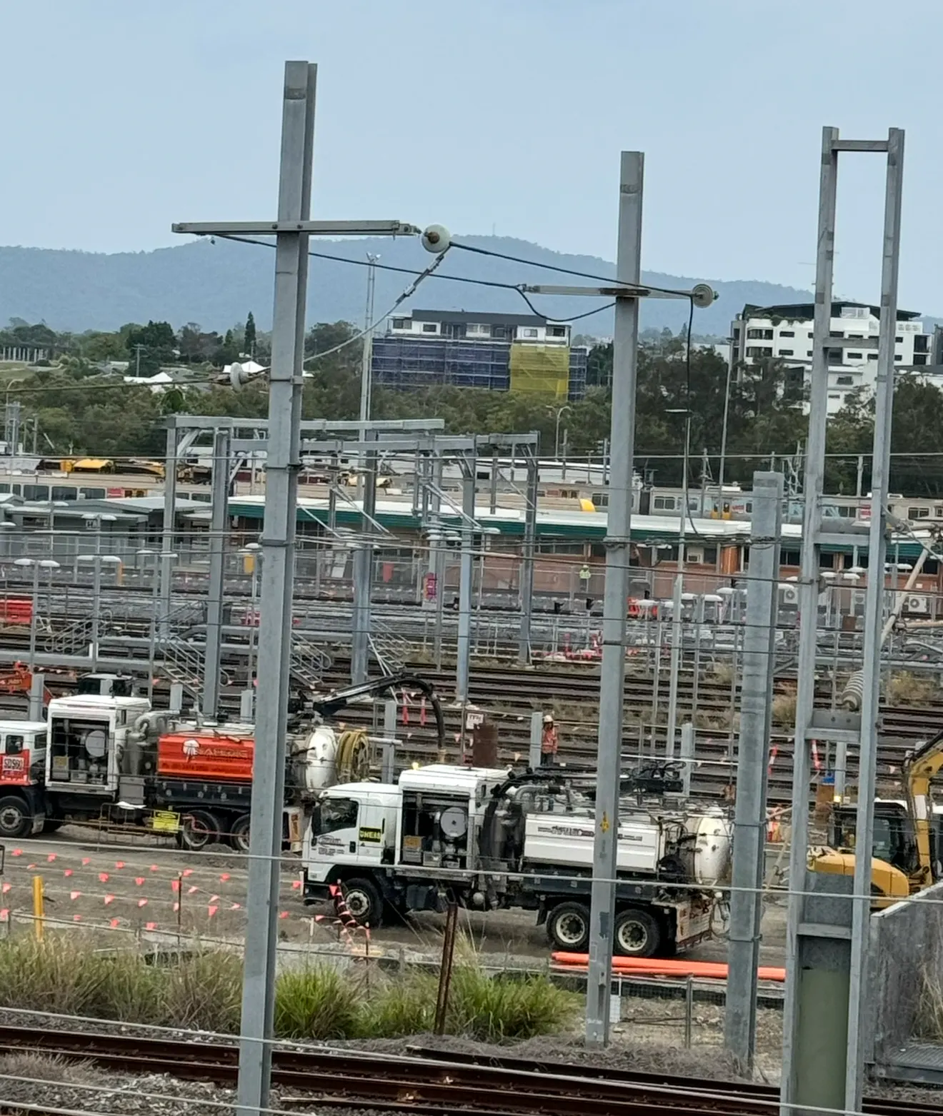 Vacuum excavation units and crew working between tracks in a rail yard beneath overhead wiring
