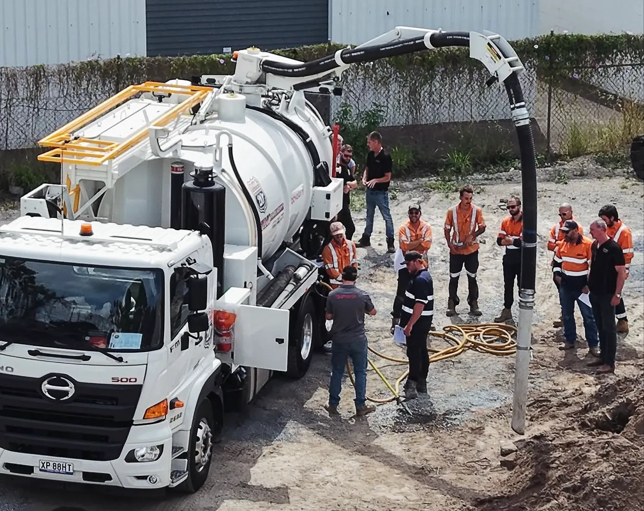 Dynamic combination unit with its boom hose lowered into a pit while the crew works alongside the truck