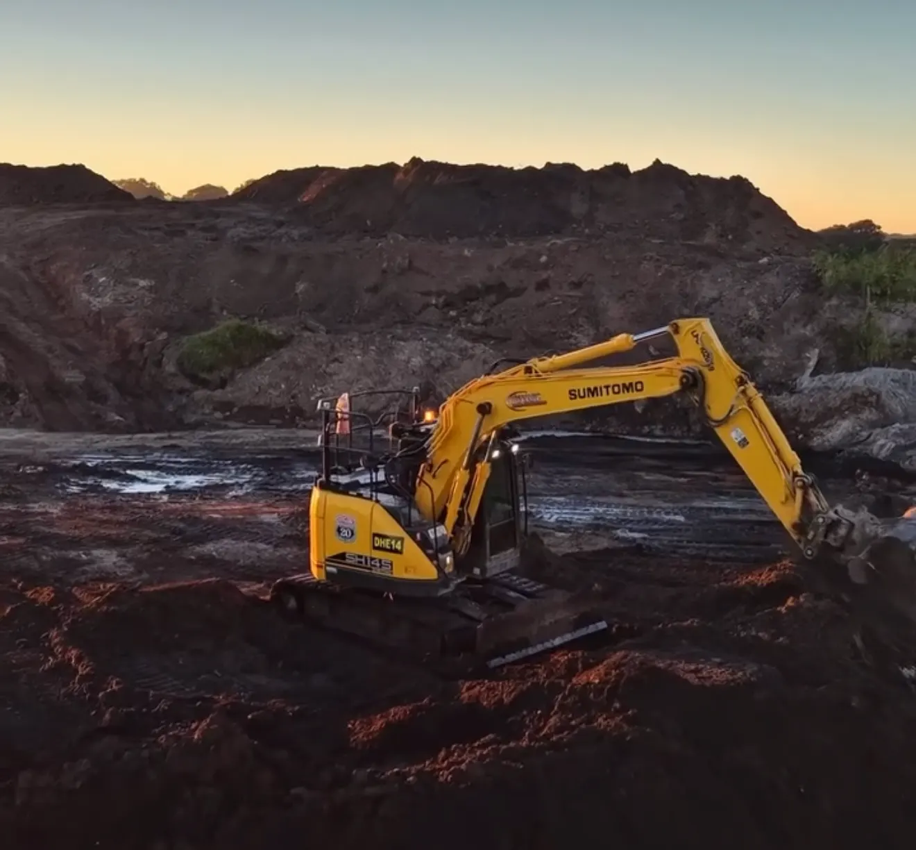 Dynamic tracked excavator working a bulk earthworks site at dusk